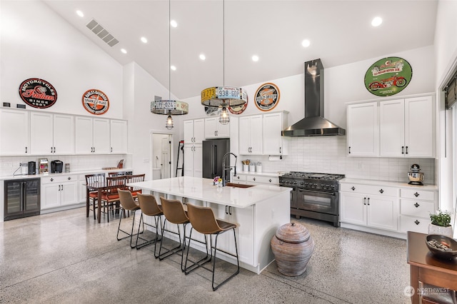 kitchen with premium appliances, wall chimney range hood, white cabinets, a breakfast bar area, and a kitchen island with sink