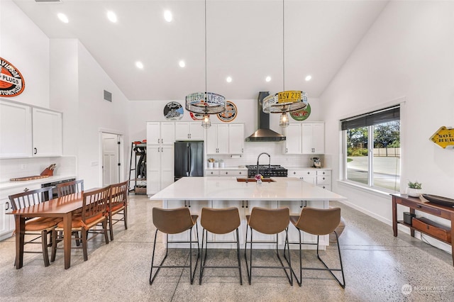 kitchen with high vaulted ceiling, freestanding refrigerator, wall chimney exhaust hood, light countertops, and light speckled floor