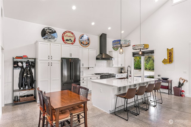 kitchen with a kitchen bar, white cabinetry, stainless steel appliances, wall chimney exhaust hood, and a kitchen island with sink