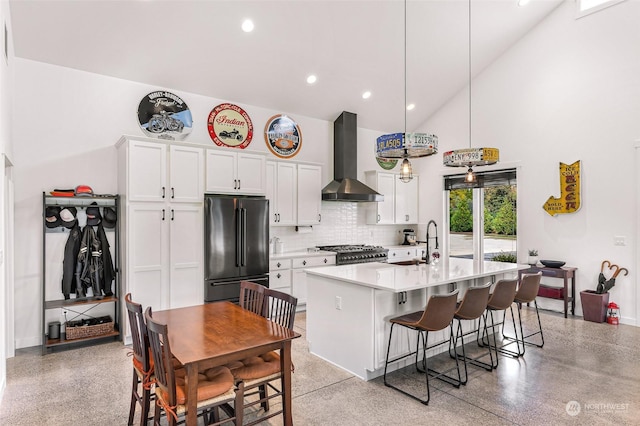 kitchen featuring a sink, decorative backsplash, high end black fridge, wall chimney range hood, and white cabinets