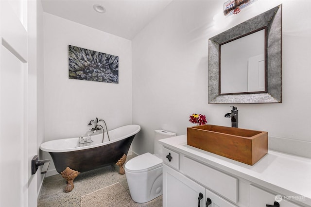 full bathroom featuring toilet, vanity, speckled floor, a freestanding bath, and baseboards