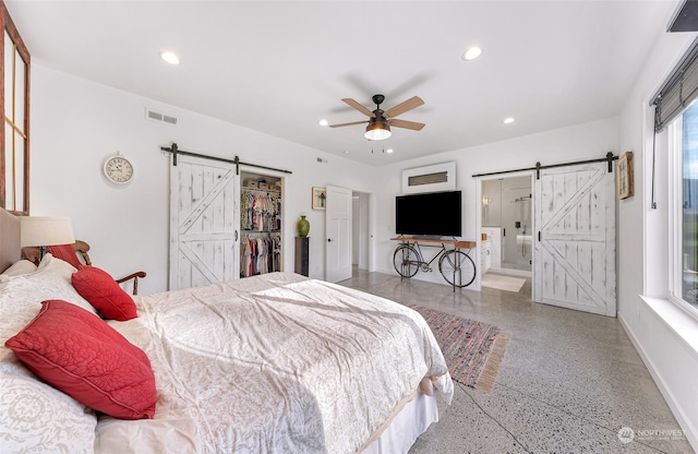 bedroom with a closet, a spacious closet, a barn door, ensuite bathroom, and ceiling fan