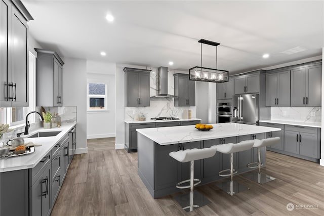 kitchen with wall chimney range hood, appliances with stainless steel finishes, a kitchen island, a kitchen breakfast bar, and pendant lighting