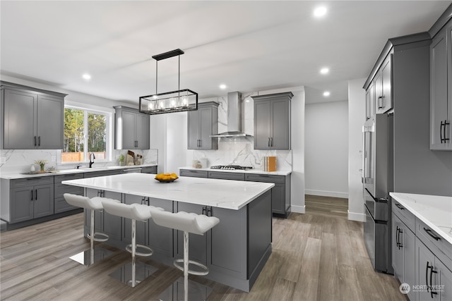 kitchen featuring a kitchen island, wall chimney exhaust hood, hanging light fixtures, gray cabinetry, and appliances with stainless steel finishes