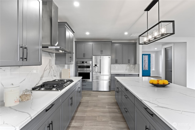 kitchen with stainless steel appliances, wall chimney exhaust hood, pendant lighting, gray cabinets, and light stone counters