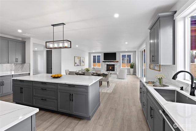 kitchen featuring a stone fireplace, sink, gray cabinets, decorative light fixtures, and light hardwood / wood-style floors