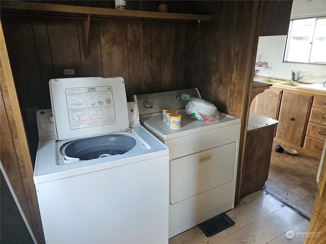 washroom with wood walls, washer and dryer, sink, and light wood-type flooring