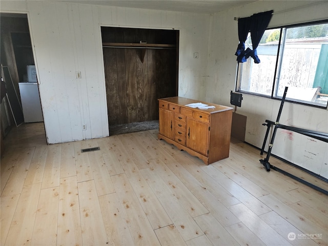 unfurnished bedroom featuring a closet, stainless steel fridge, wooden walls, and light wood-type flooring