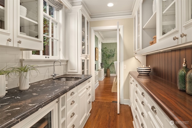 bar with sink, dark wood-type flooring, crown molding, dark stone counters, and white cabinets