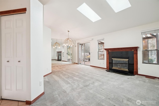 unfurnished living room featuring a tile fireplace, lofted ceiling with skylight, a chandelier, and light colored carpet