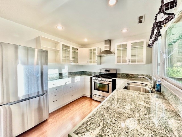 kitchen featuring appliances with stainless steel finishes, light wood-type flooring, sink, wall chimney range hood, and white cabinetry