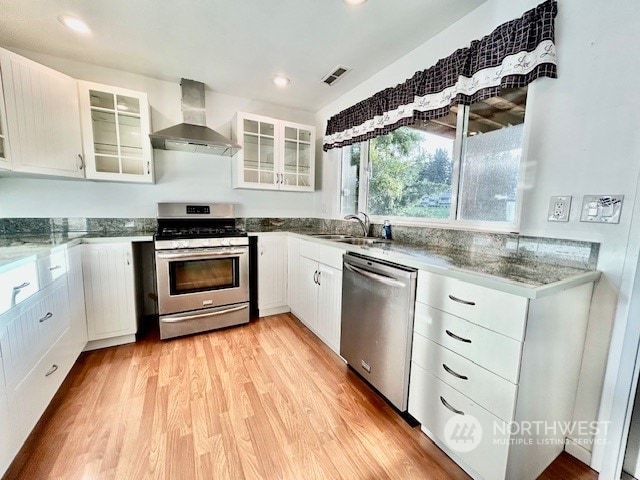 kitchen featuring wall chimney exhaust hood, plenty of natural light, white cabinetry, and appliances with stainless steel finishes