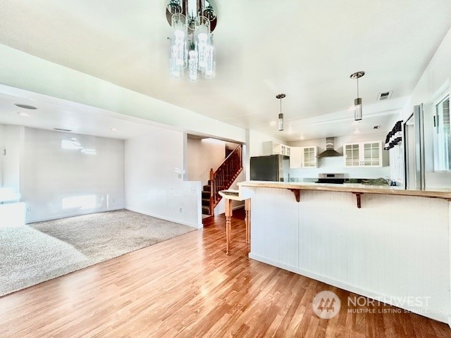 kitchen featuring wall chimney exhaust hood, light hardwood / wood-style floors, decorative light fixtures, a breakfast bar area, and black refrigerator