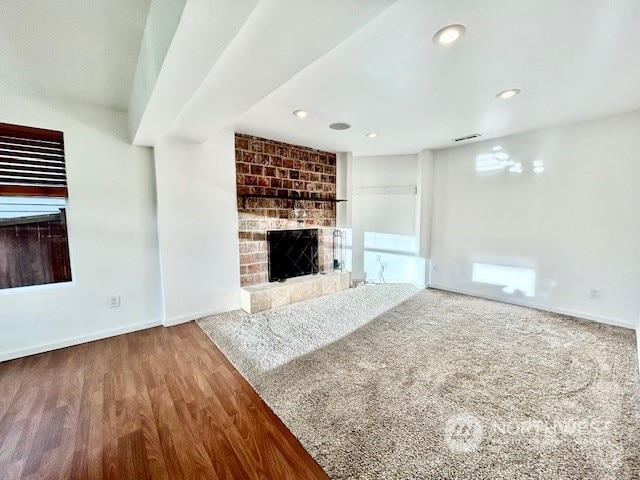 unfurnished living room featuring wood-type flooring and a brick fireplace