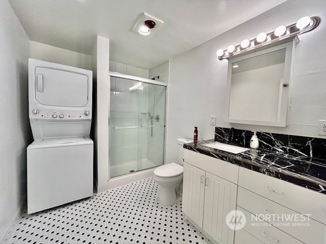 bathroom featuring vanity, a shower with shower door, stacked washer / drying machine, and toilet