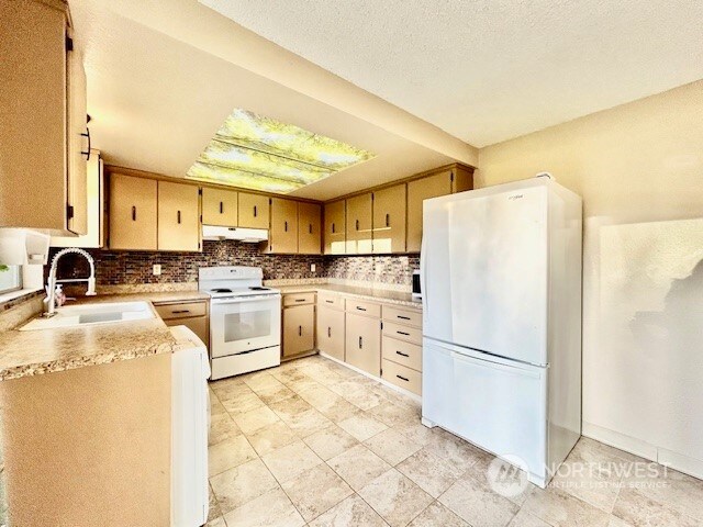 kitchen featuring decorative backsplash, a textured ceiling, white appliances, and sink