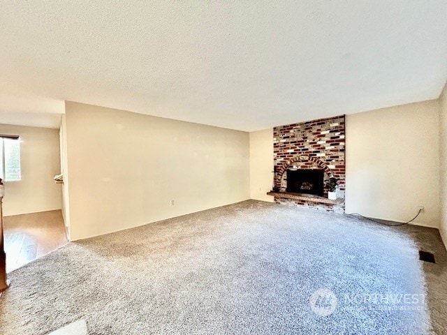 unfurnished living room featuring carpet flooring, a textured ceiling, and a brick fireplace