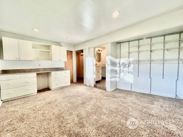 kitchen with white cabinetry, built in desk, and light carpet