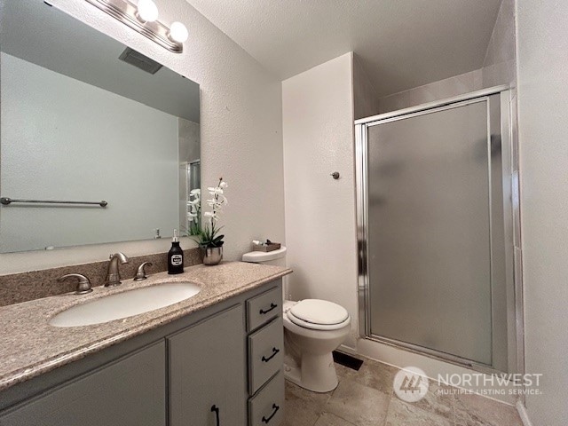 bathroom with a textured ceiling, vanity, toilet, and walk in shower