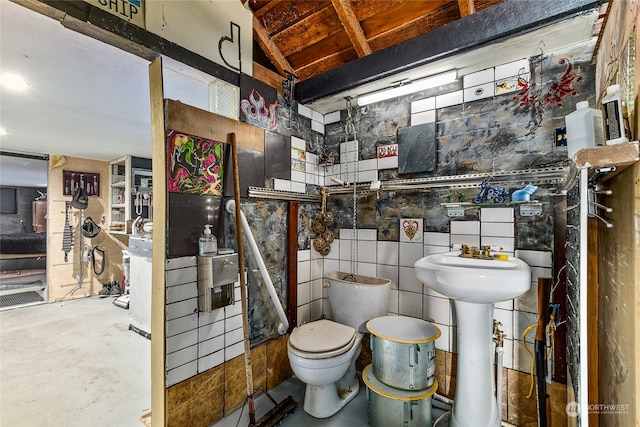 bathroom with toilet, concrete floors, and tile walls