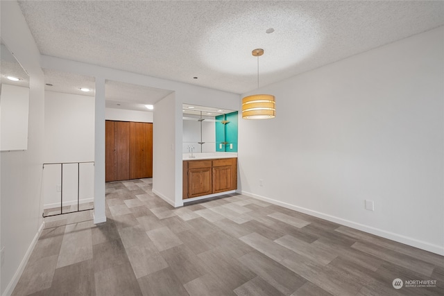 unfurnished dining area featuring sink, light hardwood / wood-style floors, and a textured ceiling