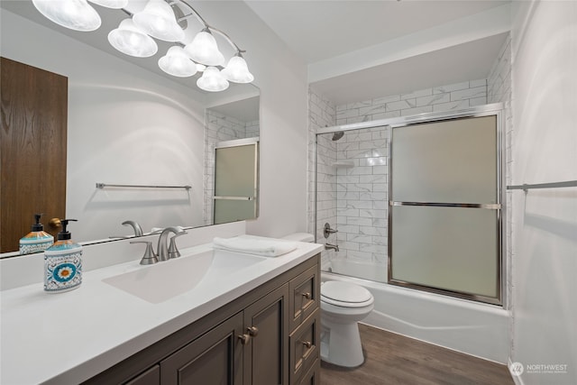 full bathroom with wood-type flooring, shower / bath combination with glass door, vanity, and toilet