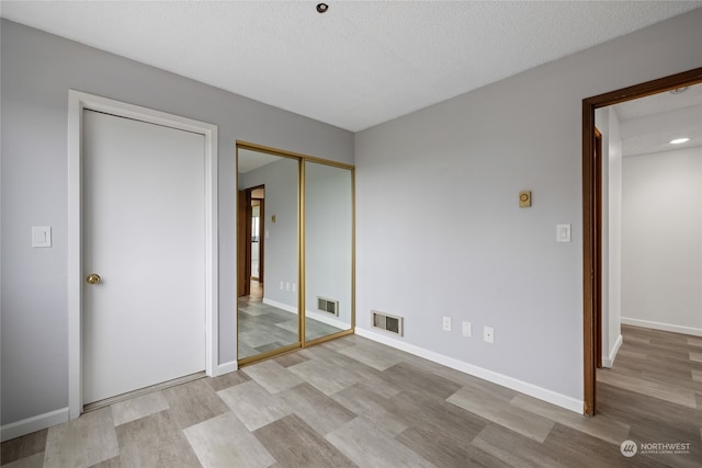 unfurnished bedroom featuring a textured ceiling, light wood-type flooring, and a closet