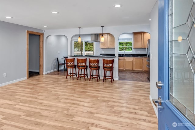 kitchen featuring sink, a kitchen bar, island range hood, hanging light fixtures, and light hardwood / wood-style flooring