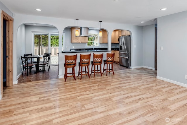 kitchen featuring a kitchen bar, light wood-type flooring, decorative light fixtures, extractor fan, and stainless steel fridge with ice dispenser