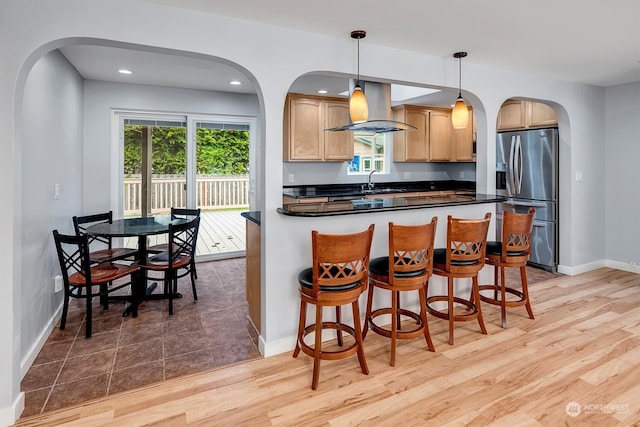 kitchen featuring ventilation hood, stainless steel fridge with ice dispenser, decorative light fixtures, and light hardwood / wood-style floors