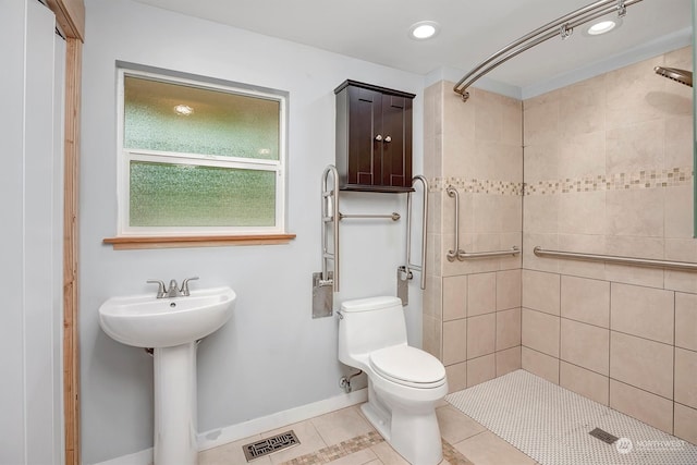 bathroom with toilet, sink, a tile shower, and tile patterned floors