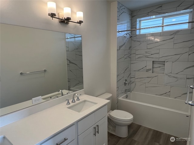 full bathroom with wood-type flooring, tiled shower / bath, vanity, and toilet