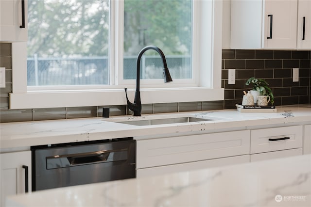 kitchen with light stone counters, dishwasher, white cabinets, and decorative backsplash