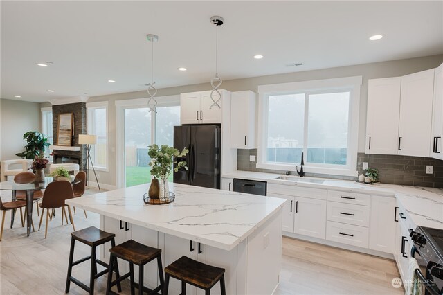 kitchen featuring hanging light fixtures, sink, black appliances, white cabinetry, and light hardwood / wood-style floors