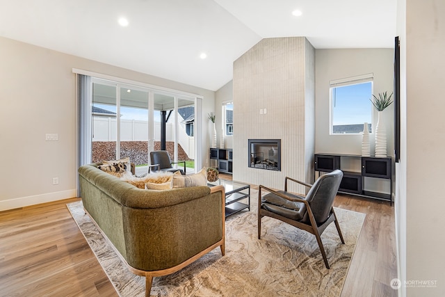 living room featuring wood-type flooring, lofted ceiling, and a tiled fireplace