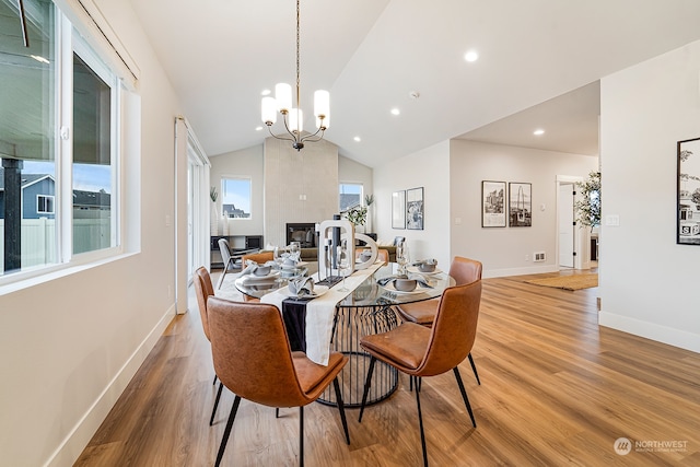 dining space featuring wood-type flooring, a notable chandelier, plenty of natural light, and vaulted ceiling