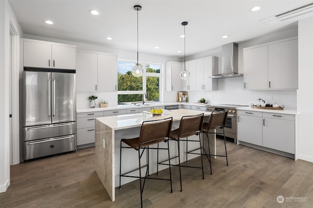 kitchen with wall chimney range hood, dark hardwood / wood-style floors, premium appliances, and a center island