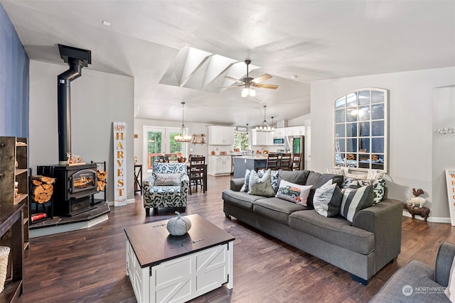 living room featuring a wood stove, dark wood-type flooring, ceiling fan with notable chandelier, and vaulted ceiling