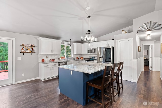 kitchen featuring appliances with stainless steel finishes, a center island, white cabinets, dark wood-type flooring, and light stone counters