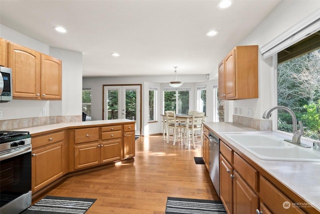 kitchen with pendant lighting, sink, stainless steel appliances, light wood-type flooring, and french doors