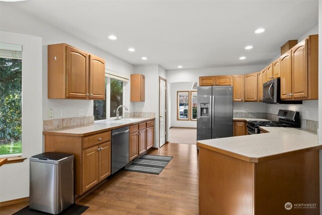 kitchen with appliances with stainless steel finishes, kitchen peninsula, sink, and light wood-type flooring