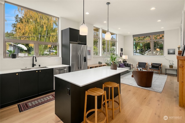 kitchen featuring pendant lighting, sink, light hardwood / wood-style flooring, stainless steel appliances, and a center island