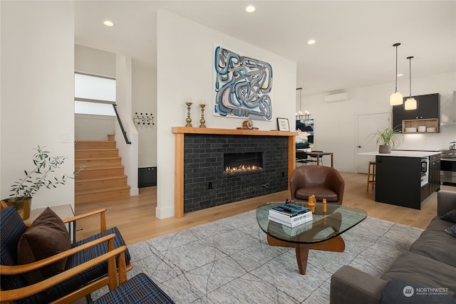 living room with a brick fireplace, an inviting chandelier, light wood-type flooring, and a wall mounted AC