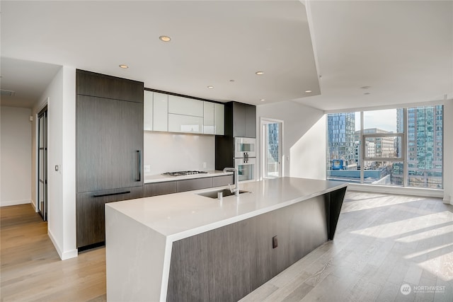 kitchen featuring a center island with sink, sink, white gas cooktop, and light wood-type flooring