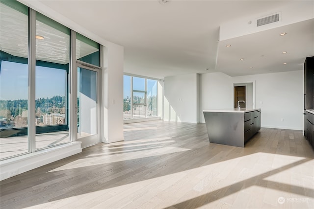 kitchen with floor to ceiling windows, a center island with sink, and light wood-type flooring