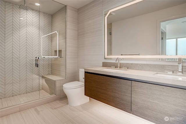 bathroom with vanity, toilet, tile walls, and a shower with shower door