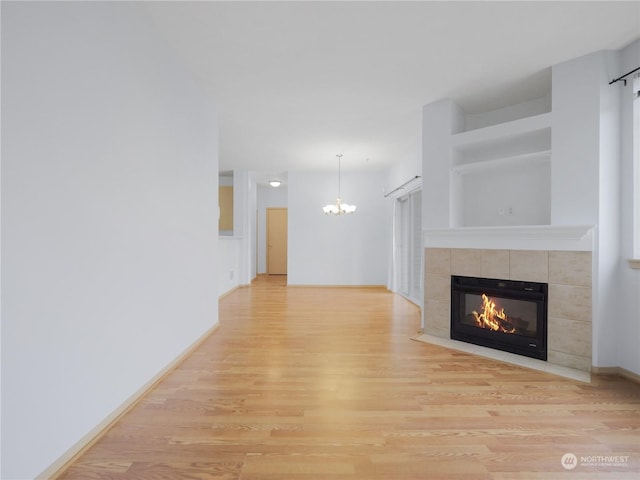 unfurnished living room with a tiled fireplace, light hardwood / wood-style floors, and an inviting chandelier