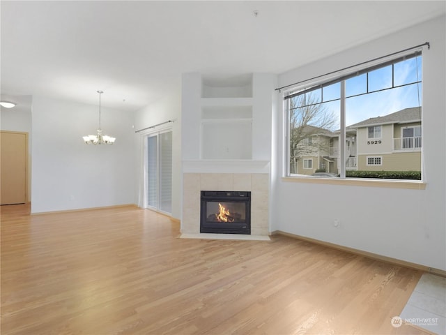 unfurnished living room with a tile fireplace, an inviting chandelier, and light hardwood / wood-style floors