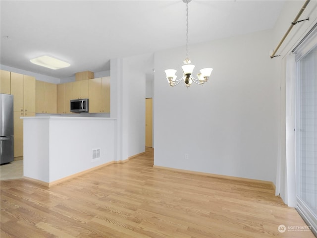 kitchen with hanging light fixtures, stainless steel appliances, a notable chandelier, cream cabinets, and light hardwood / wood-style floors