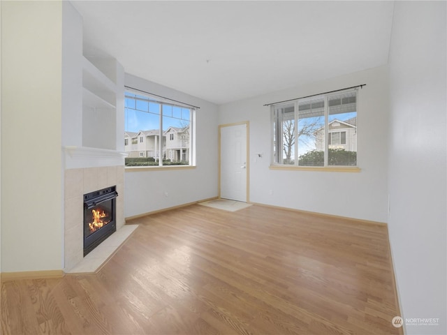 unfurnished living room featuring a tiled fireplace, light wood-type flooring, and a wealth of natural light